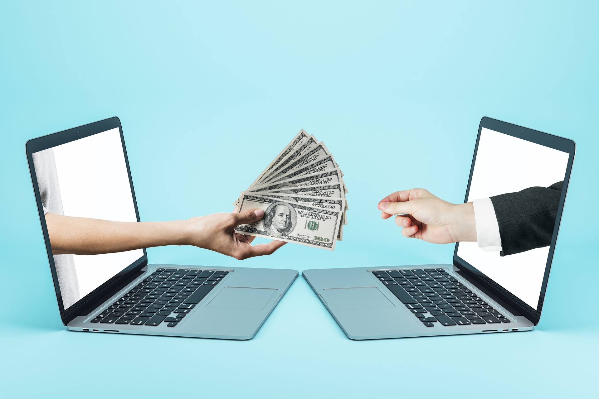 Hand passes a wad of dollars through laptops screens